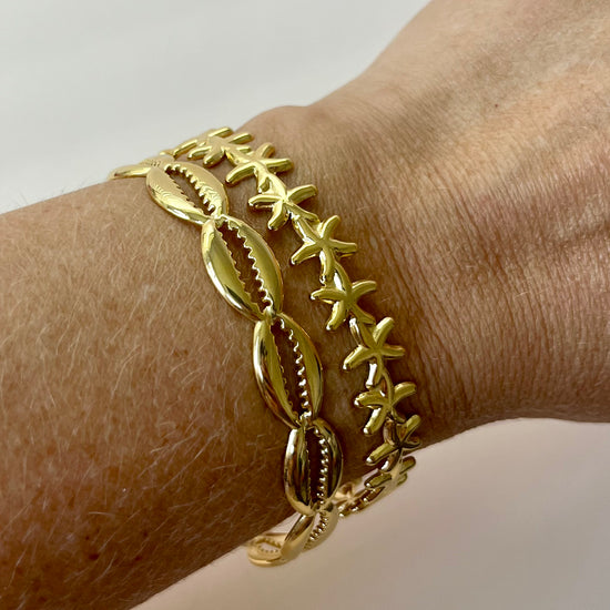 Two gold bangle bracelets featuring a tropical cowrie shell and a delicate starfish charm. Made from waterproof, non-tarnish stainless steel—perfect for coastal styling, summer outfits, or vacation-ready jewelry collections.