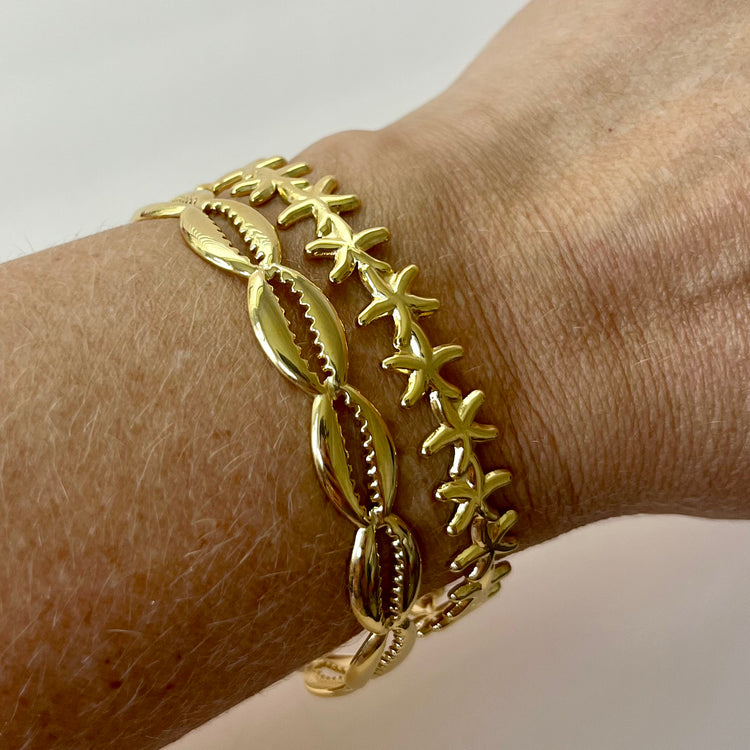 Two gold bangle bracelets featuring a tropical cowrie shell and a delicate starfish charm. Made from waterproof, non-tarnish stainless steel—perfect for coastal styling, summer outfits, or vacation-ready jewelry collections.