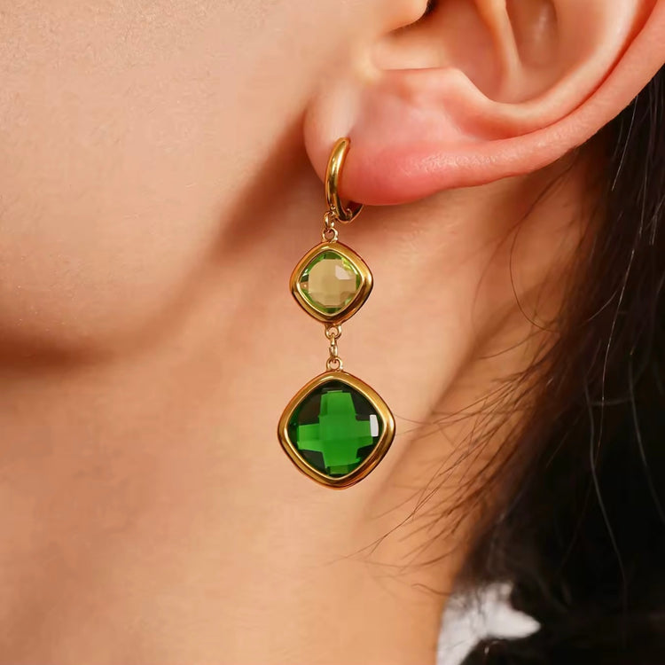 Gold earring with green gemstones worn by a person