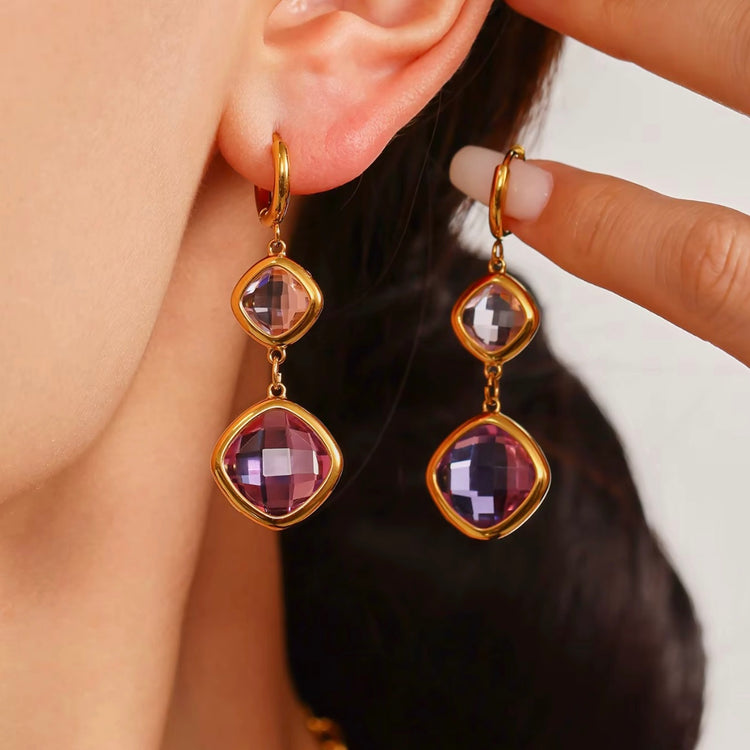 Gold earrings with purple gemstones worn by a person