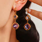Gold earrings with purple gemstones worn by a person