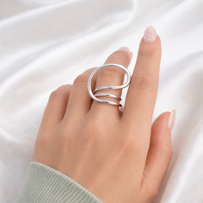 Silver Sam spiral adjustable ring on hand with soft white silk background, minimalist wrap design.