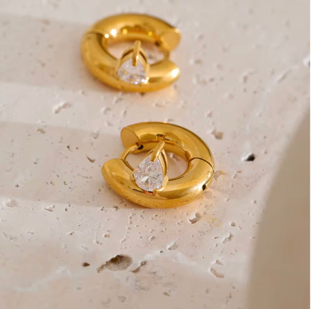 Elle Huggies gold teardrop cubic zirconia huggie earrings on neutral stone surface