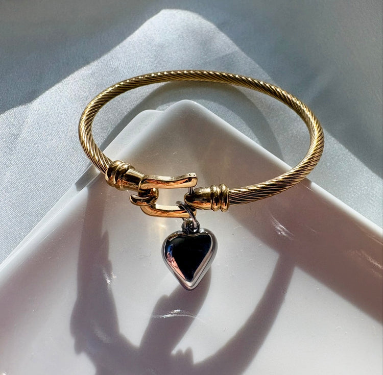 Gold bracelet with a heart-shaped black pendant on a white surface