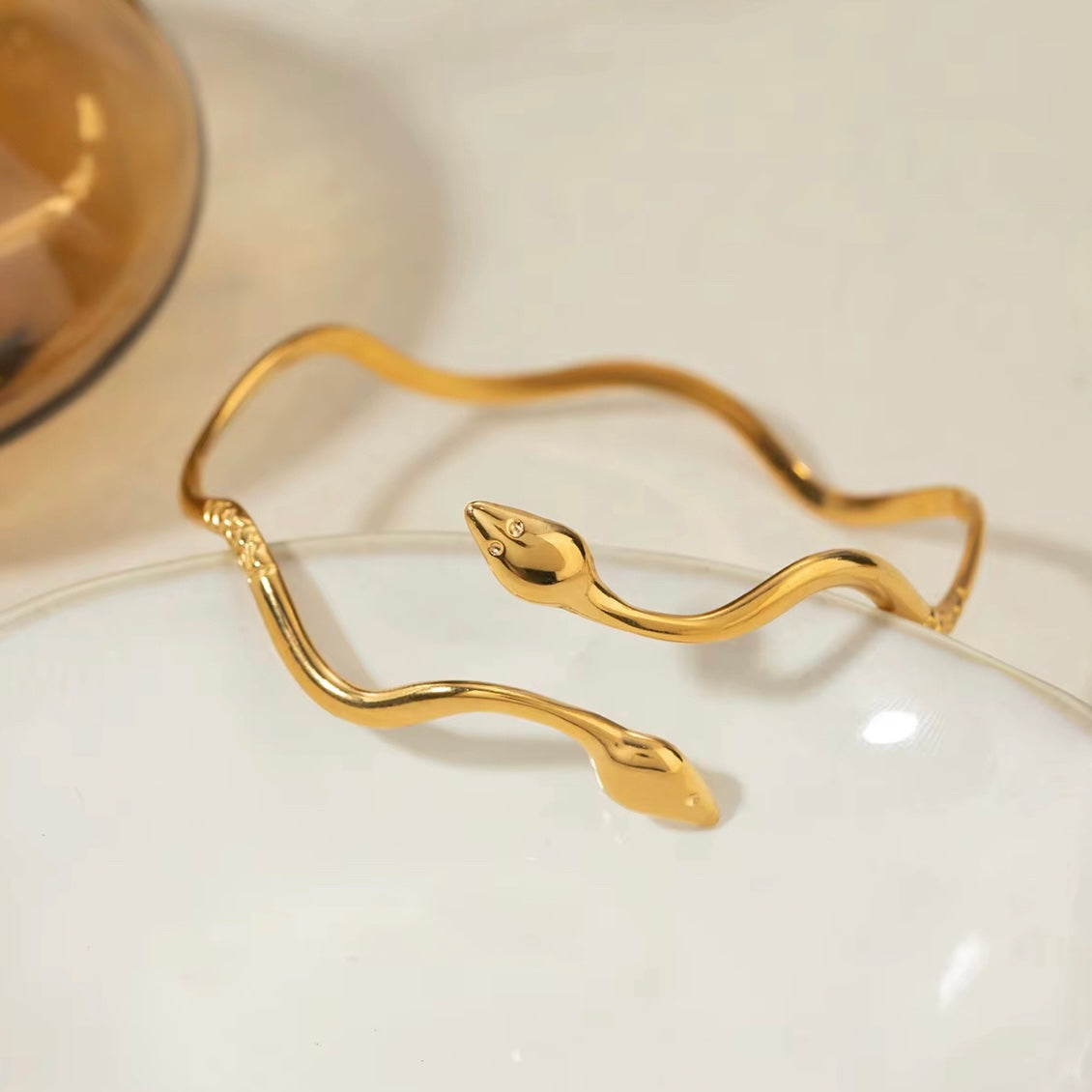 Non-tarnish snake bracelet with dual heads leaning against a plate