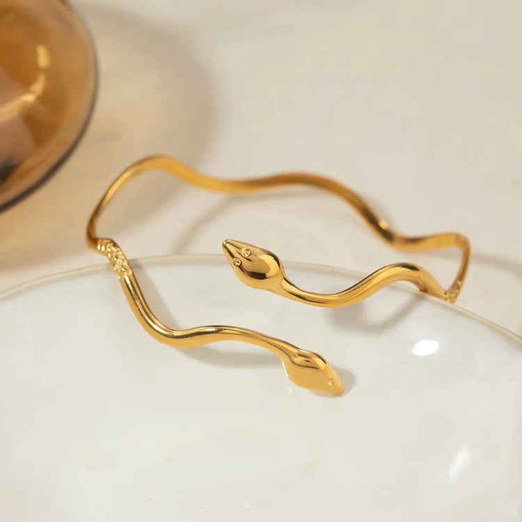 Non-tarnish snake bracelet with dual heads leaning against a plate
